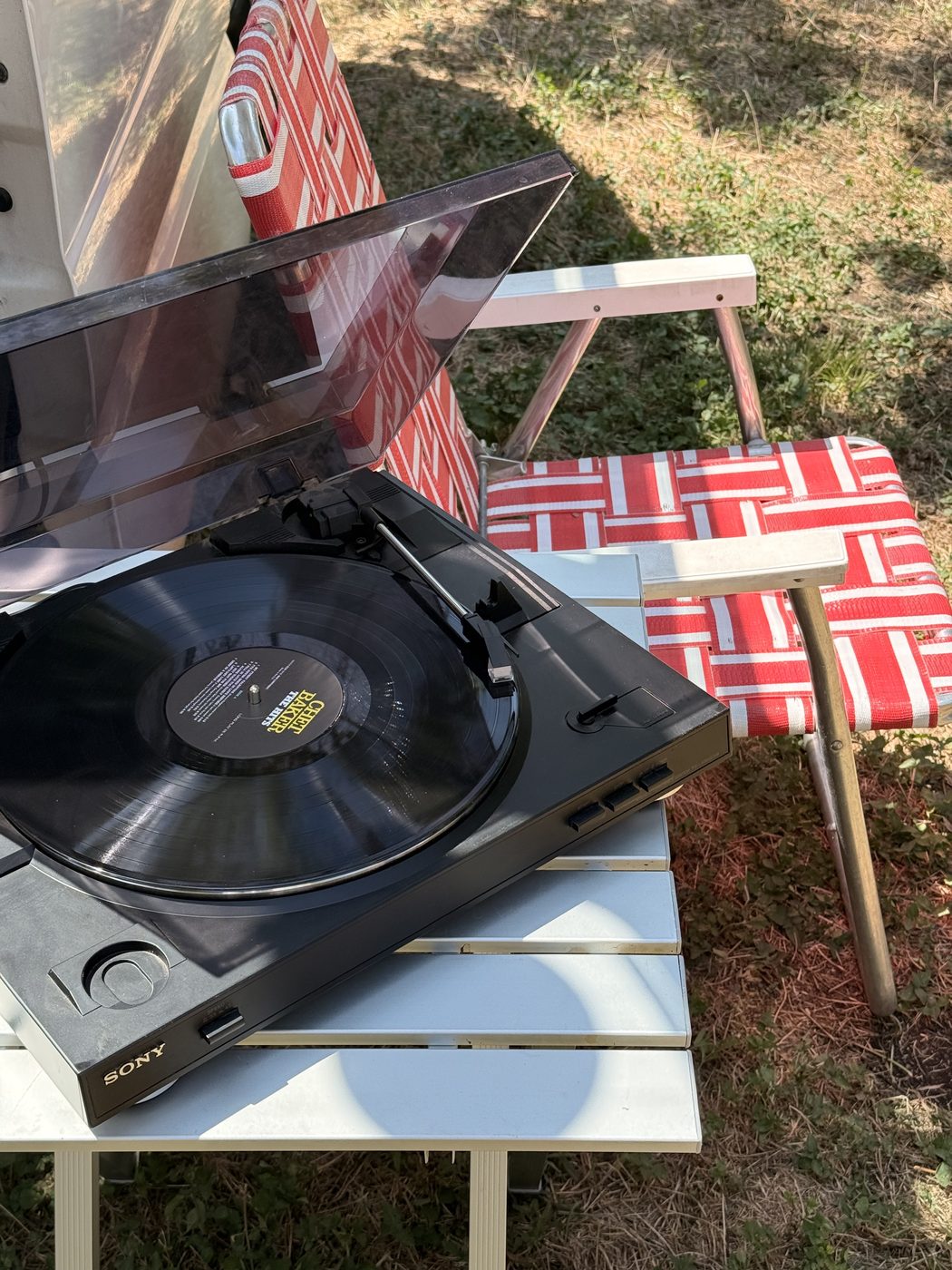 A turntable on the grass, with a red and white lawn chair beside it.